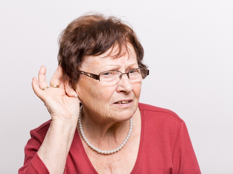 Eine schwerhörige Frau, hält sich die Hand vors Ohr, um besser hören zu können.