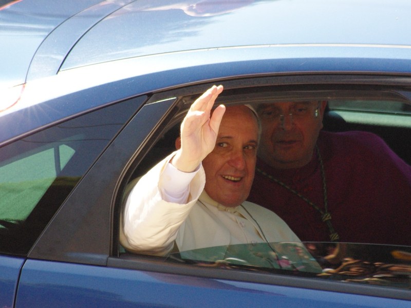 Der Papst sitzt in einem Auto und winkt aus dem Fenster.