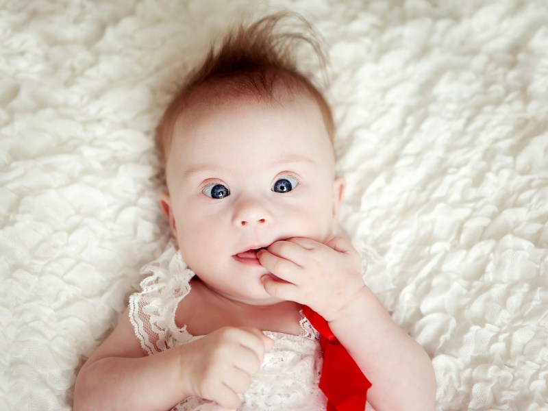 Ein niedliches Baby mit Downsyndrom liegt auf einer Decke.