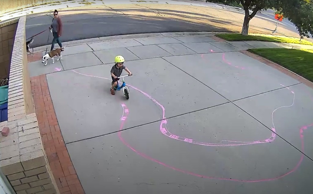 Ein Kind fährt mit seinem Fahrrad einen mit Kreide gemalten Parkour in einer Einfahrt.