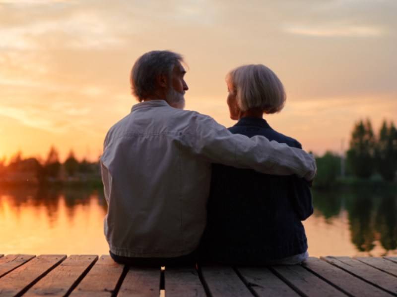 Altes Ehepaar sitzt zusammen am Seeufer und genießt den schönen Sonnenuntergang.