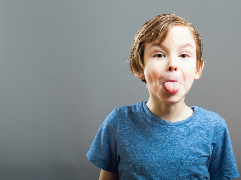 Ein frecher blonder Junge streckt die Zunge heraus.