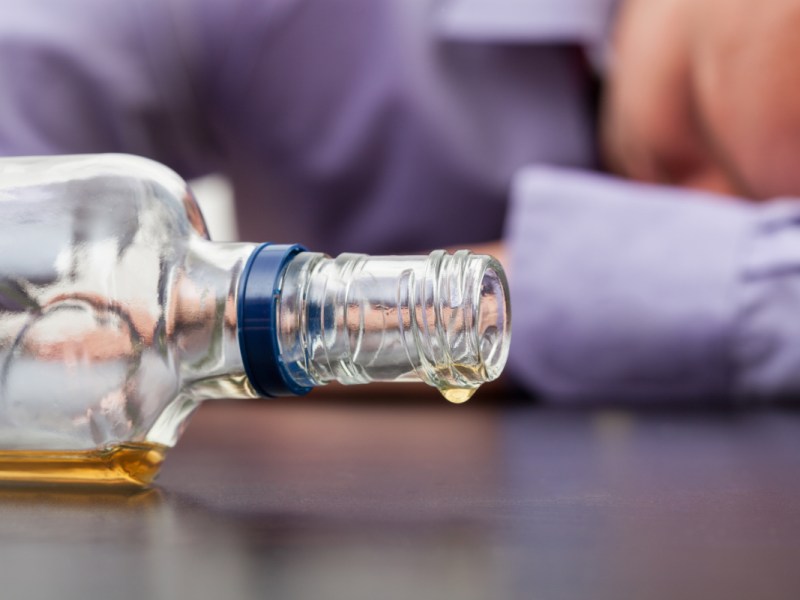 Ein betrunkener Mann schläft neben einer leeren Alkohol-Flasche.