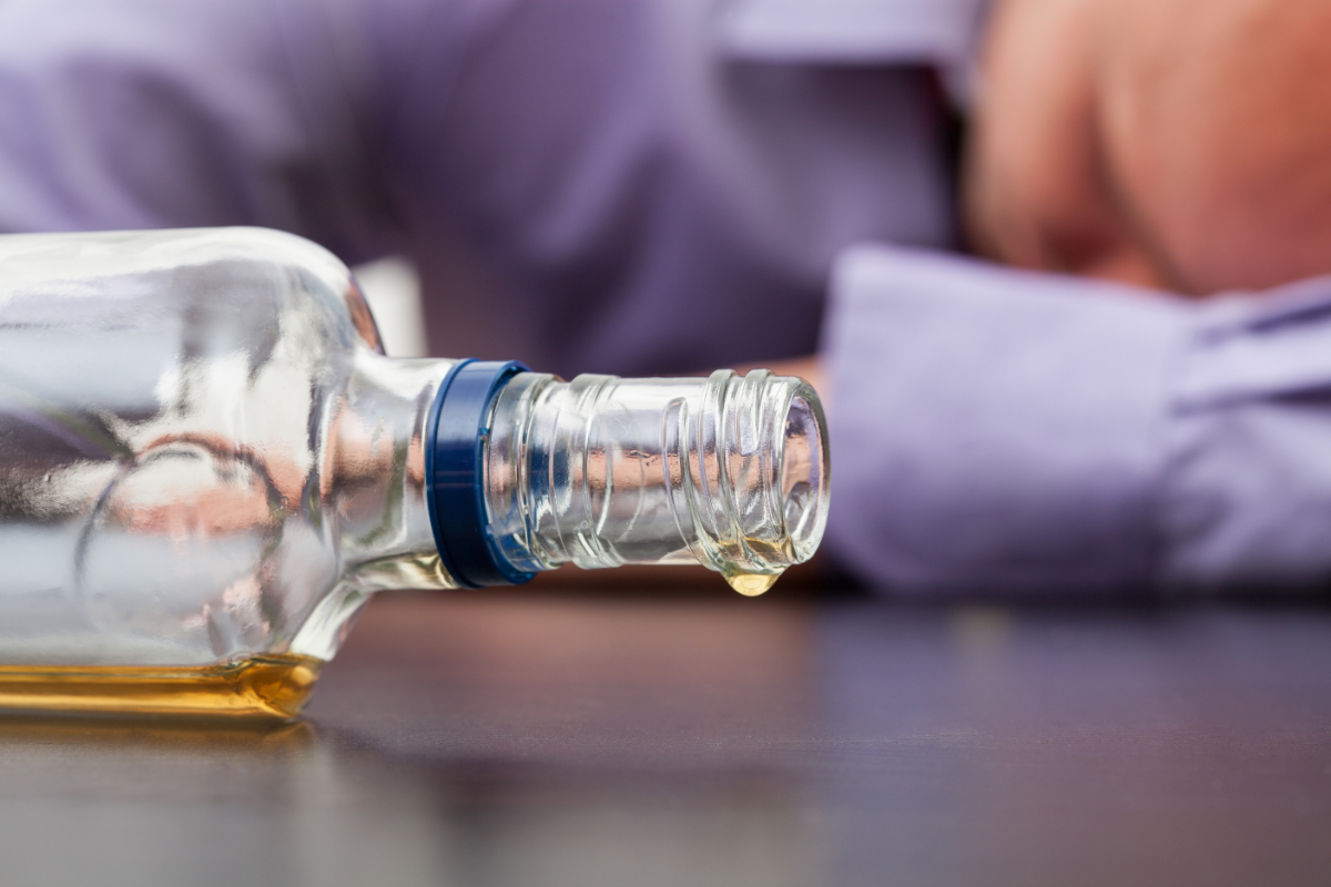 Ein betrunkener Mann schläft neben einer leeren Alkohol-Flasche.